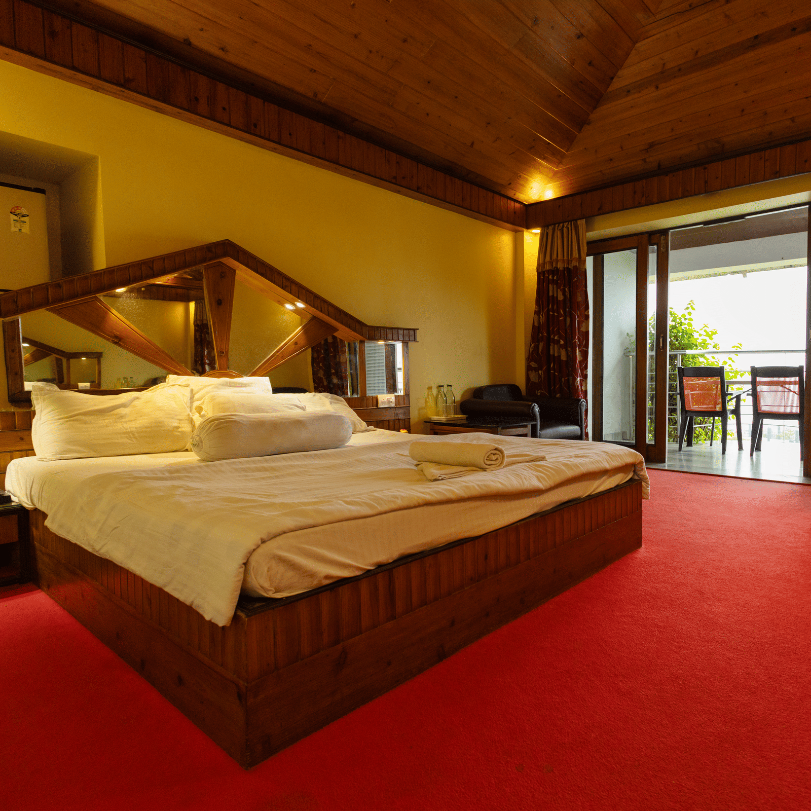 A bedroom with a king size bed, seating area, red carpet, and open balcony door at Hotel Seagull Digha.